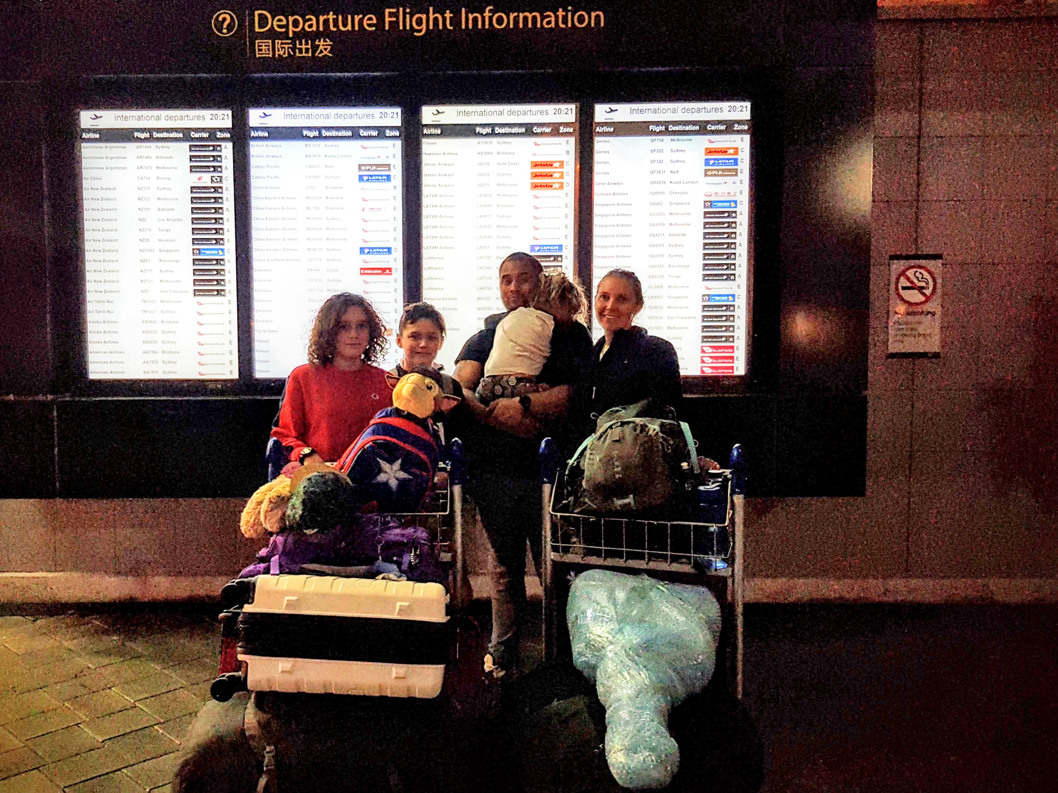 Family at Auckland Airport departure board before Vietnam flight - World Travel Ambitions