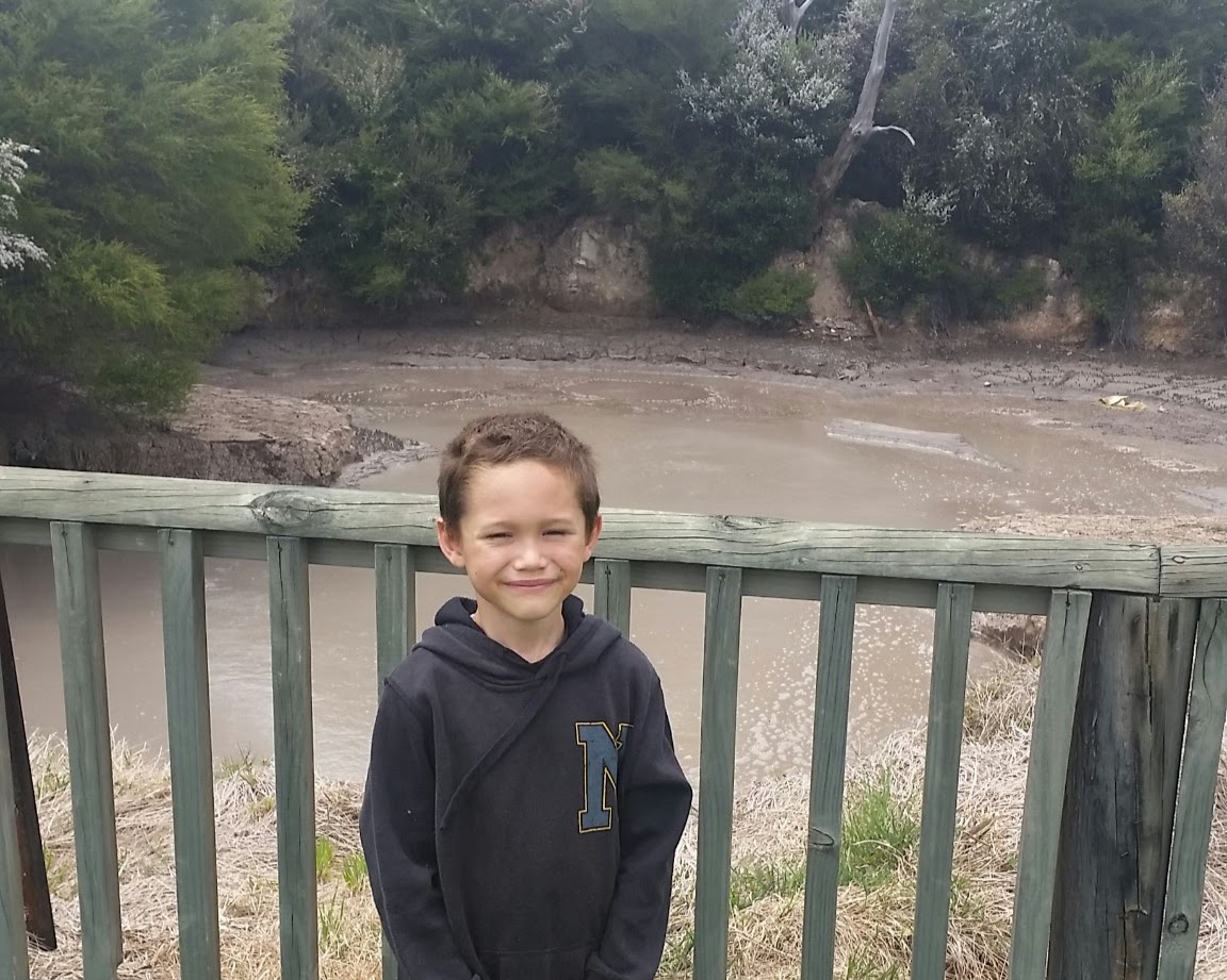 Young boy at Kuirau Park mud pools in Rotorua showing geothermal activity and wooden safety railings