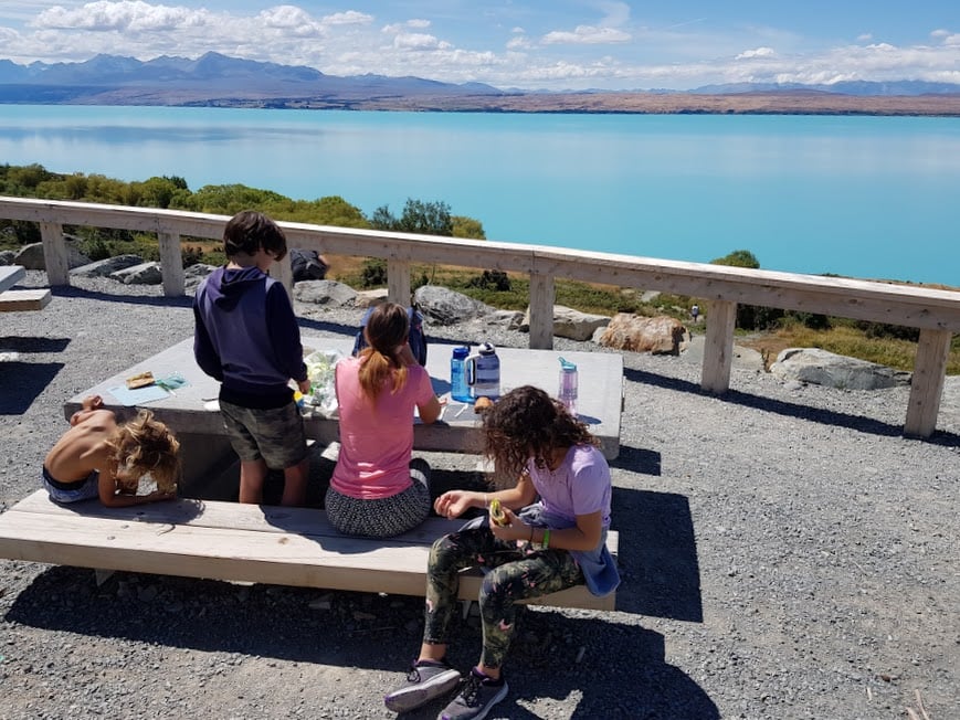 Family enjoying picnic lunch at Peter's Lookout with stunning view of turquoise Lake Pukaki and snow-capped mountains in New Zealand