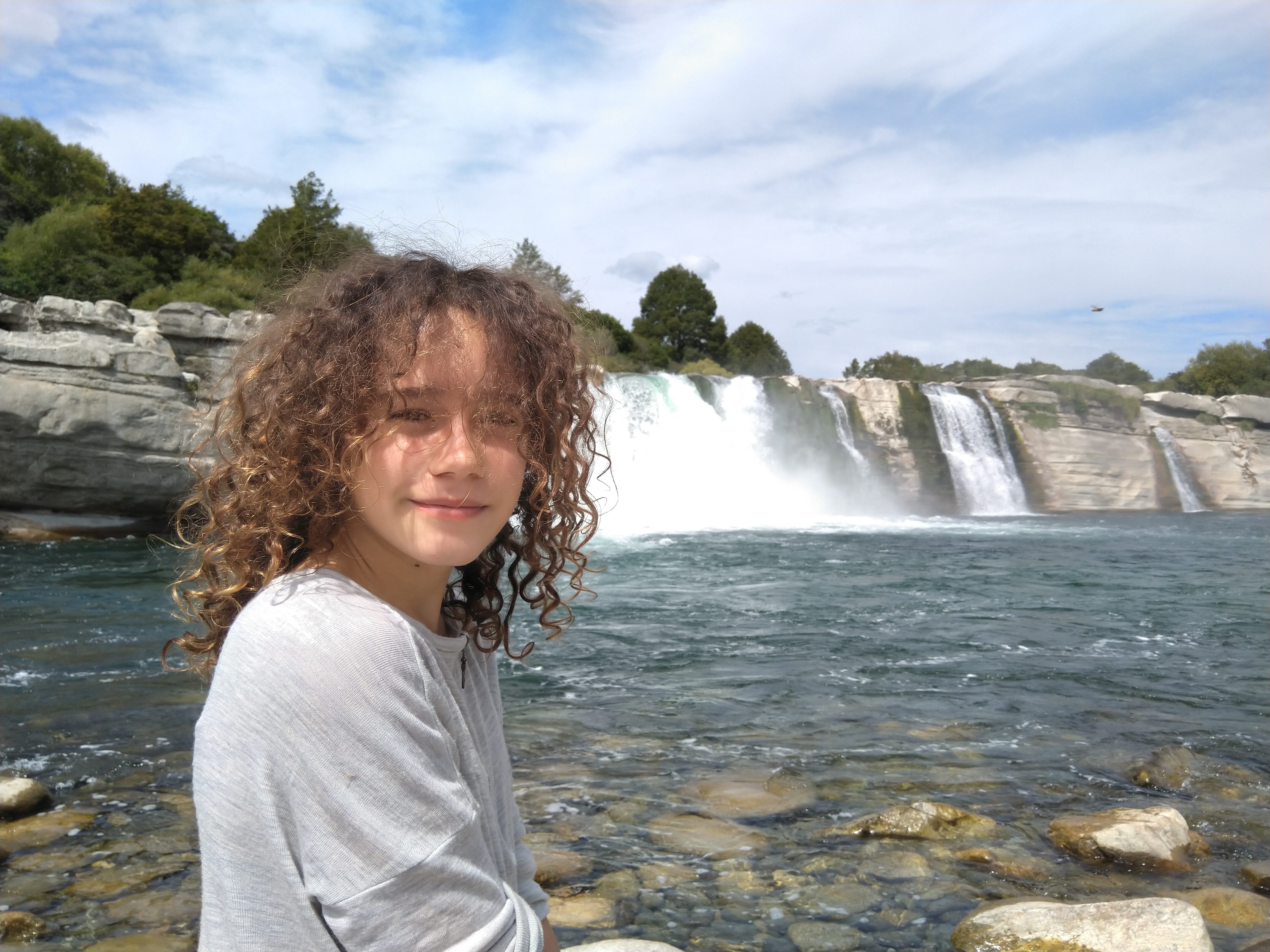 Family member enjoying the view at Maruia Falls with powerful waterfall cascading over rocky ledge in New Zealand