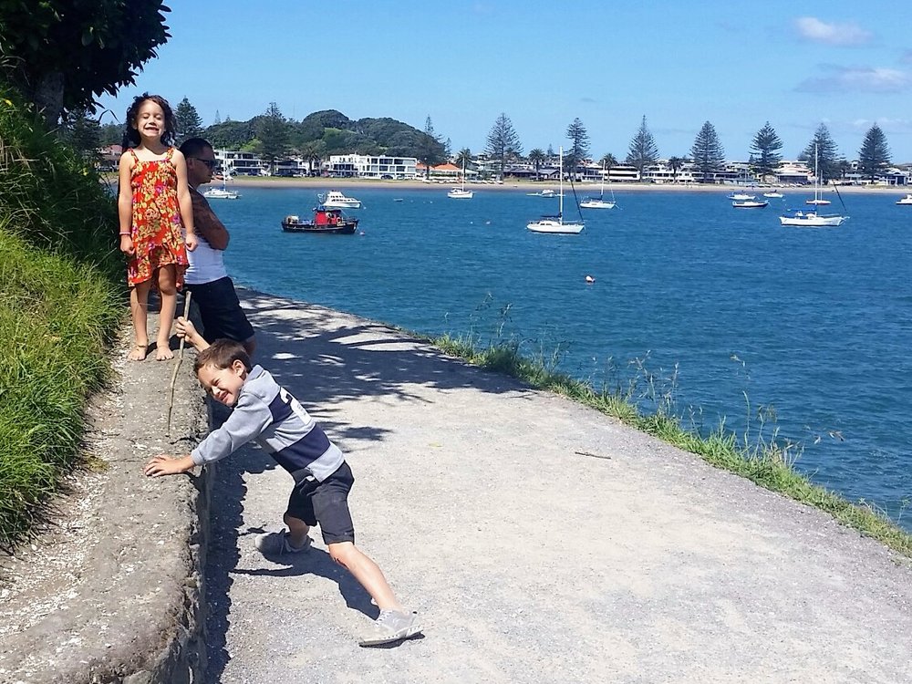 Family enjoying a walk along the Mount Maunganui base track with beautiful harbor views and sailboats