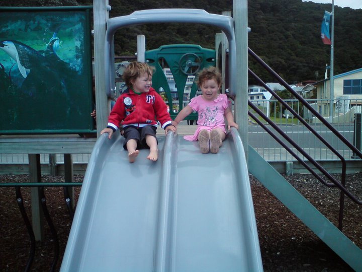 Children playing on a playground slide in Paihia with beautiful hills and town in the background