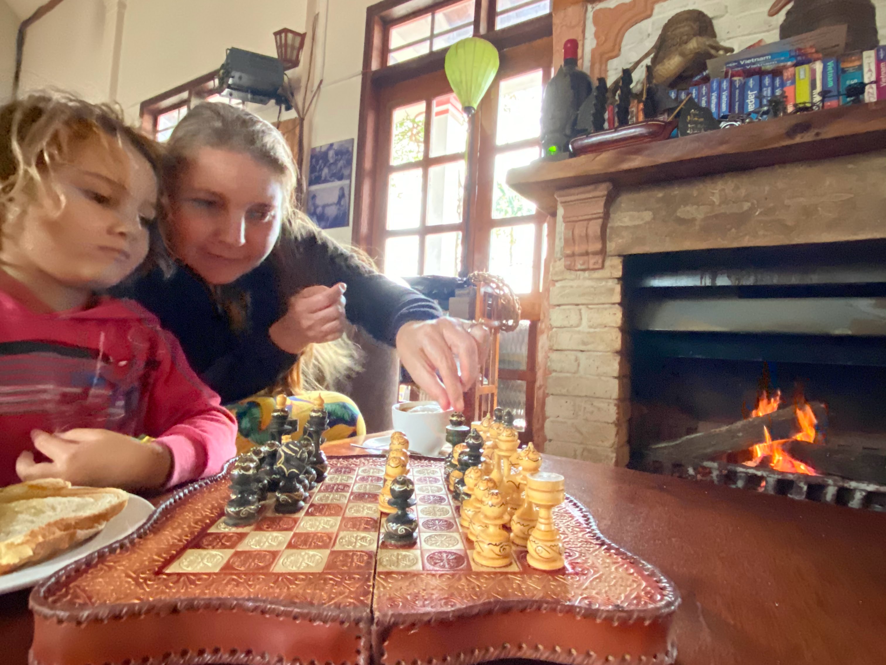 Cozy indoor scene with woman and child playing chess by a warm fireplace in Phong Nha, Vietnam - showing the cooler months when families gather indoors