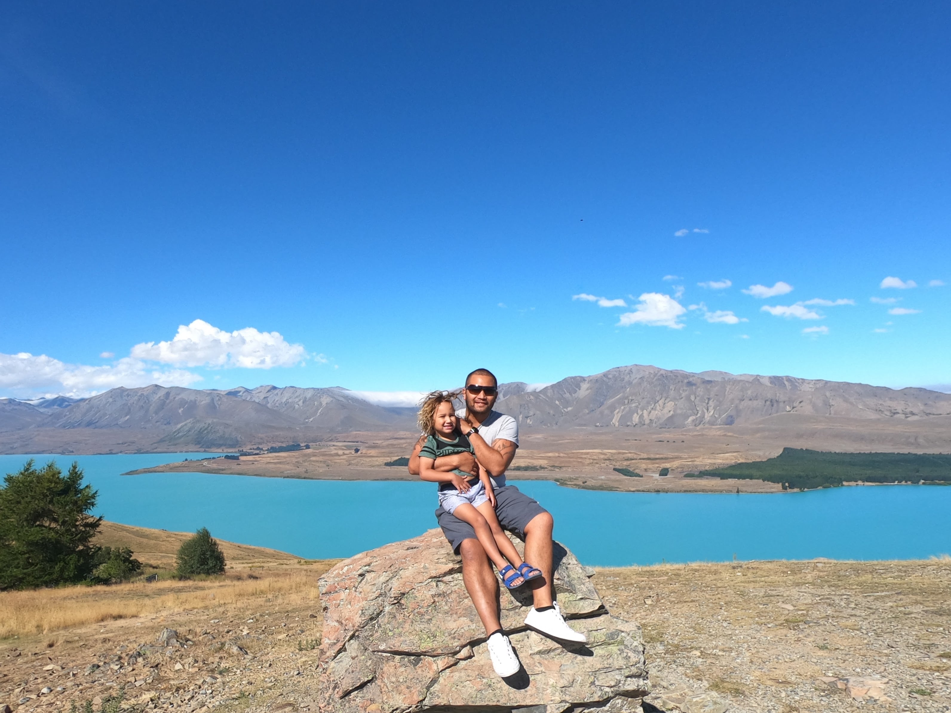 Father and child enjoying breathtaking view from Tekapo Observatory with turquoise lake and snow-capped mountains in New Zealand