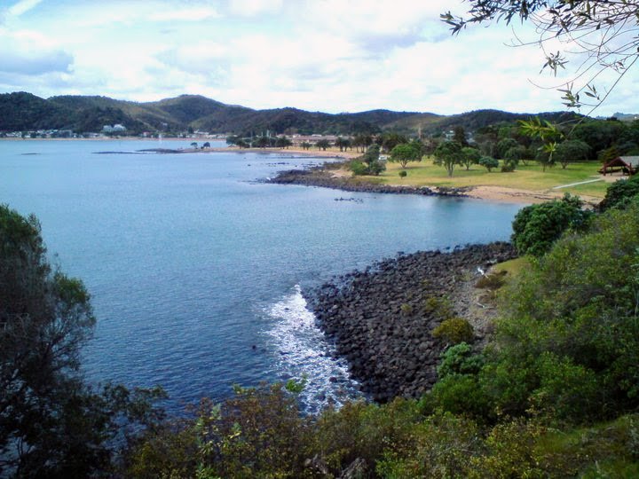 Scenic view from Waitangi Treaty Grounds showing the Bay of Islands with calm blue water, rocky coastline, sandy beaches, and rolling green hills in the background