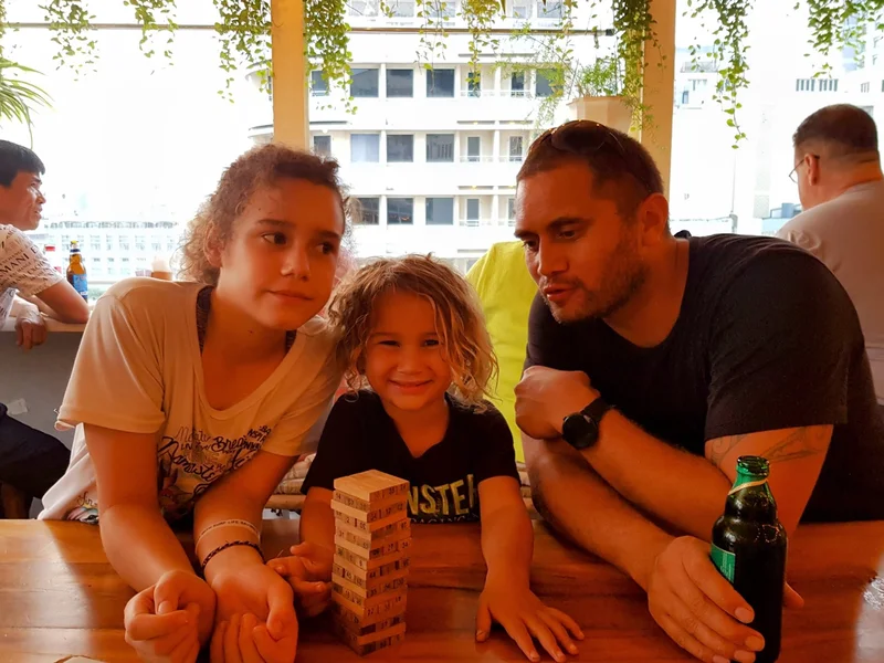Family playing Jenga at Vo Roof Garden in Saigon with city skyline in the background and green foliage hanging above
