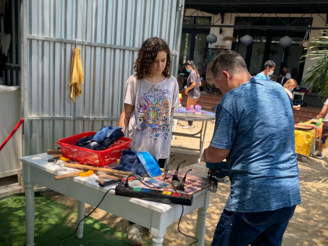 Worldschooling community workshop in Hoi An, Vietnam 2021 - families and children working together on creative projects with tools and materials on outdoor tables